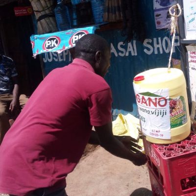 A man in a red t-shirt bends over to wash his hands to prevent the spread of COVID19 at a stand in Kibera Nairobi