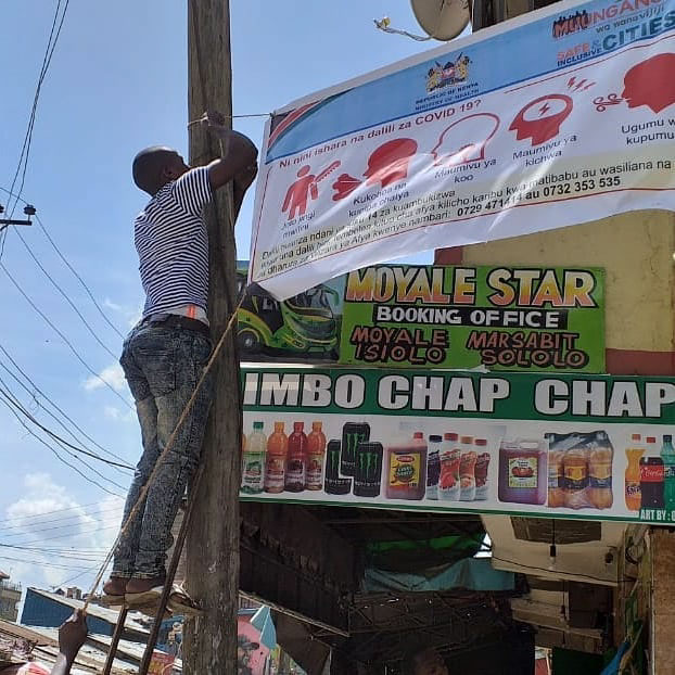 Youth from Huruma puts up a Covid-19 information banner around one of the settlements major roads by Know Your City Tv.