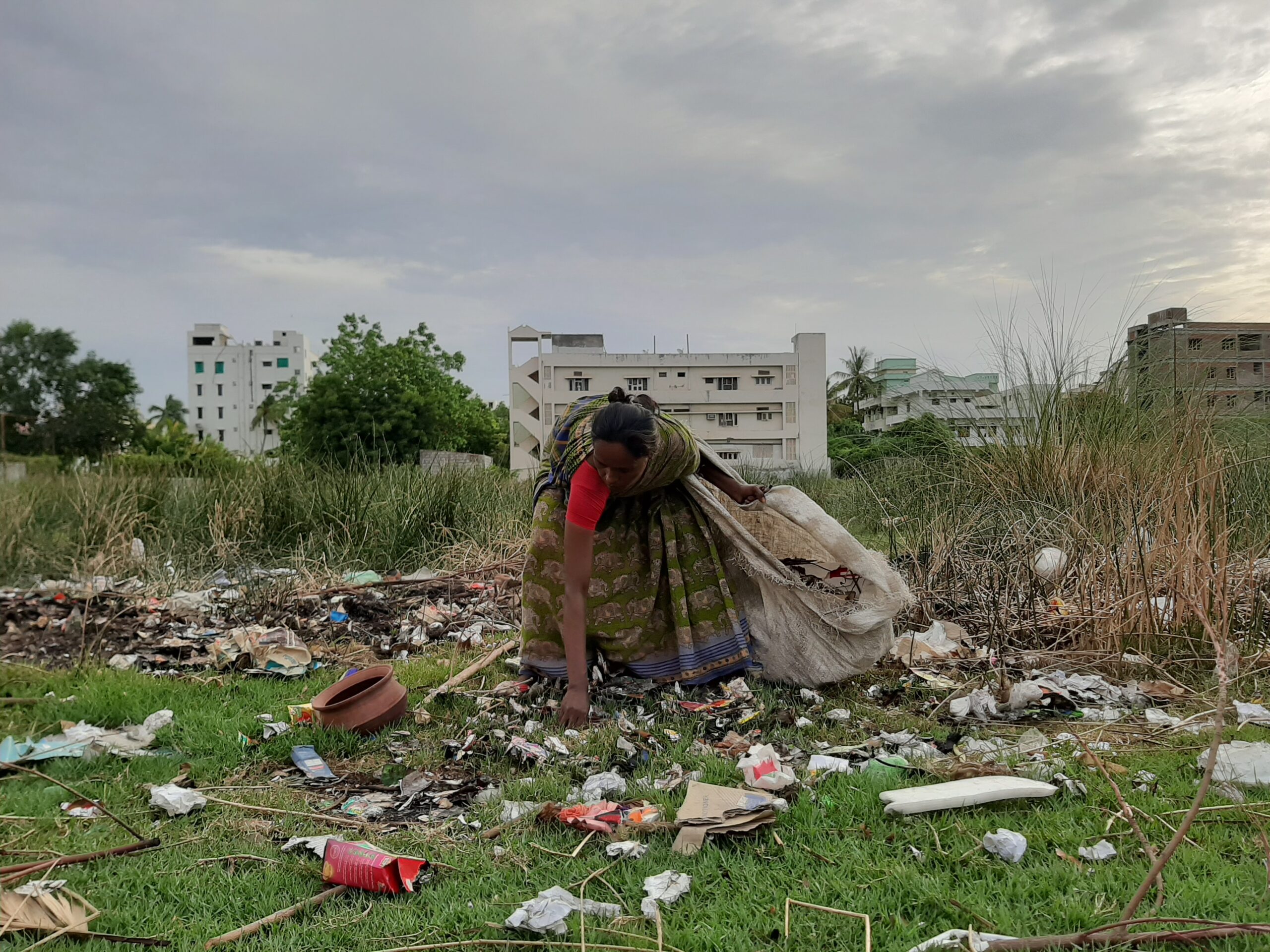 Suvartha bending to pick up rubbish in front of imposing colony buildings