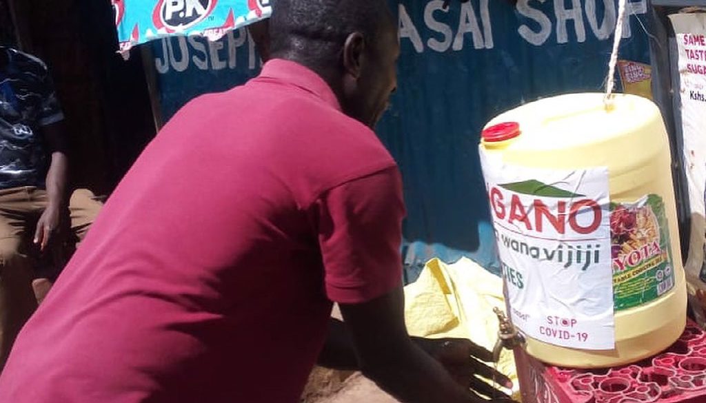 A man in a red t-shirt bends over to wash his hands to prevent the spread of COVID19 at a stand in Kibera Nairobi