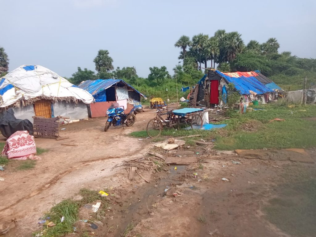 Drainage canal in foreground with informal housing and trees in background