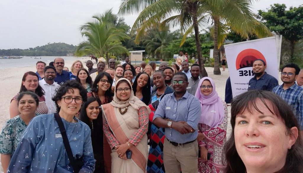 Group photograph of ARISE colleagues outside near the sea at the AGM